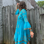 A woman wearing the Cotton Crepe Lace Embroidery Turquoise Dress in front of a wooden fence.