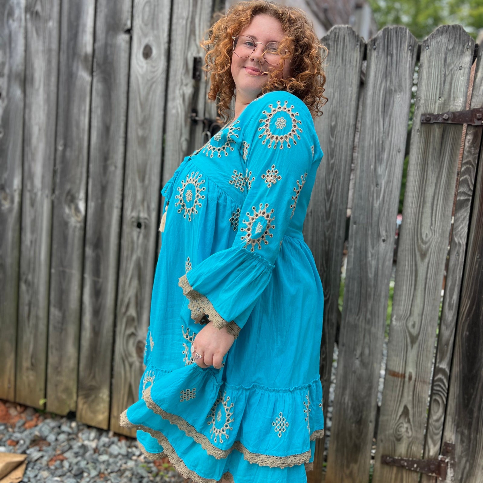 A woman wearing the Cotton Crepe Lace Embroidery Turquoise Dress in front of a wooden fence.