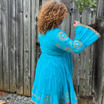 A woman wearing the Cotton Crepe Lace Embroidery Turquoise Dress in front of a wooden fence.