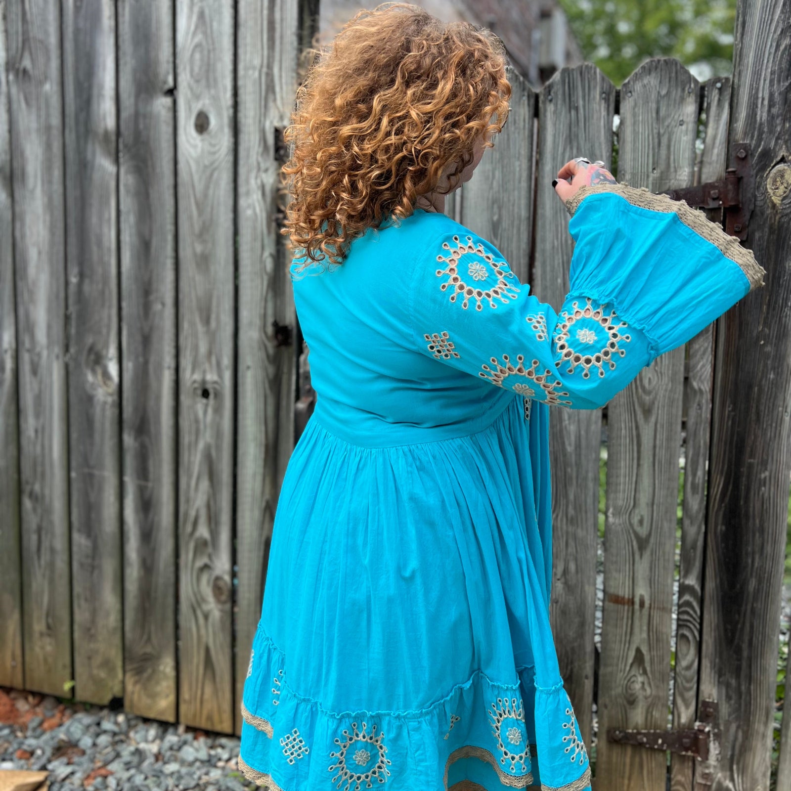A woman wearing the Cotton Crepe Lace Embroidery Turquoise Dress in front of a wooden fence.