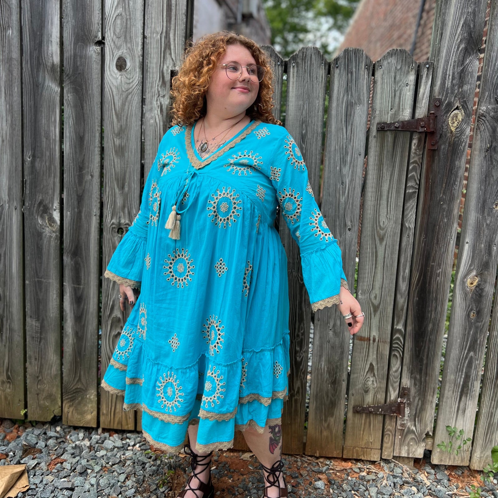 A woman wearing the Cotton Crepe Lace Embroidery Turquoise Dress in front of a wooden fence.