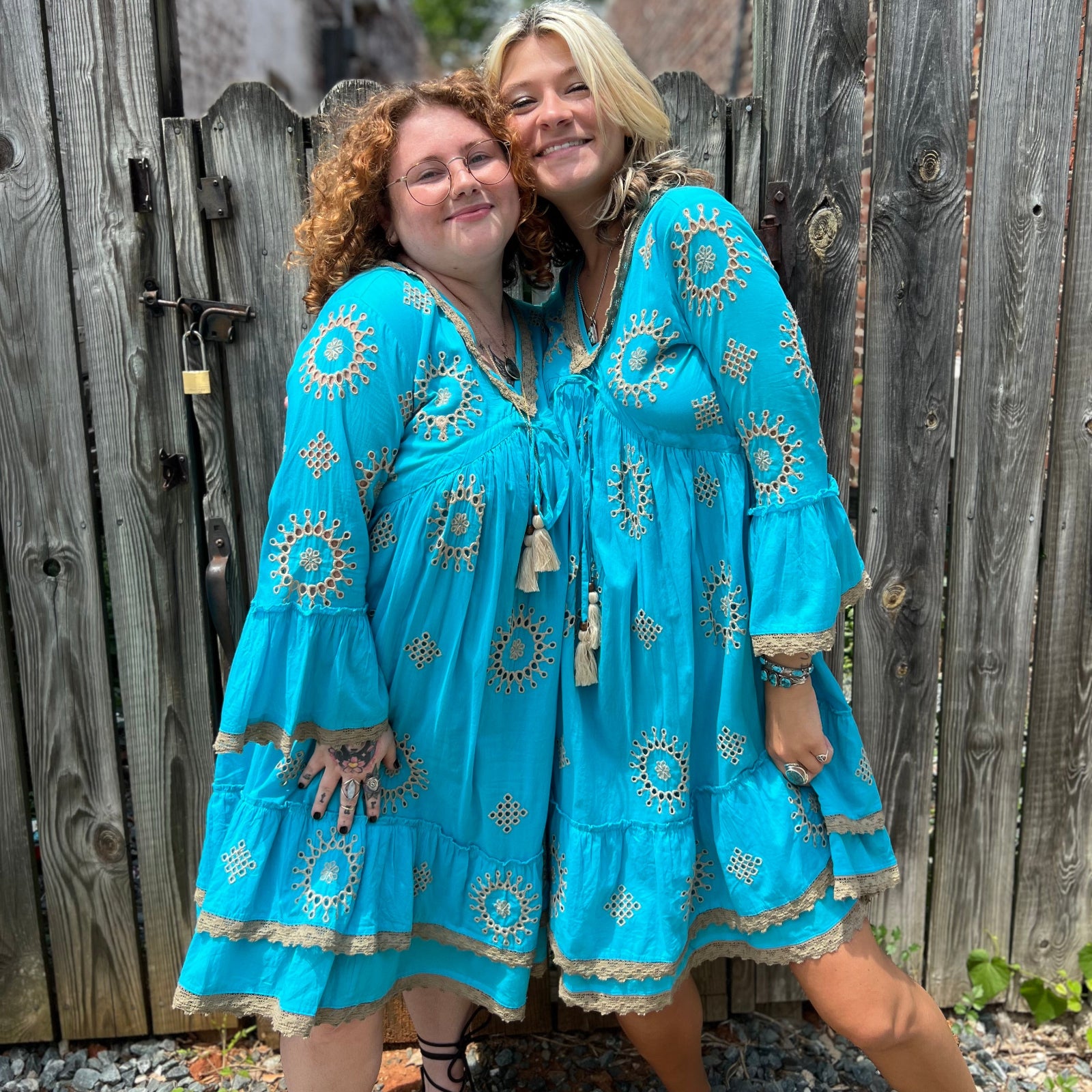 Two women wearing the Cotton Crepe Lace Embroidery Turquoise Dresses in front of a wooden fence.