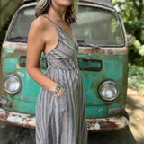 A woman wearing the Grey Striped Palazzo Cotton Jumpsuit in front of a vintage Volkswagen bus, showing off the side.