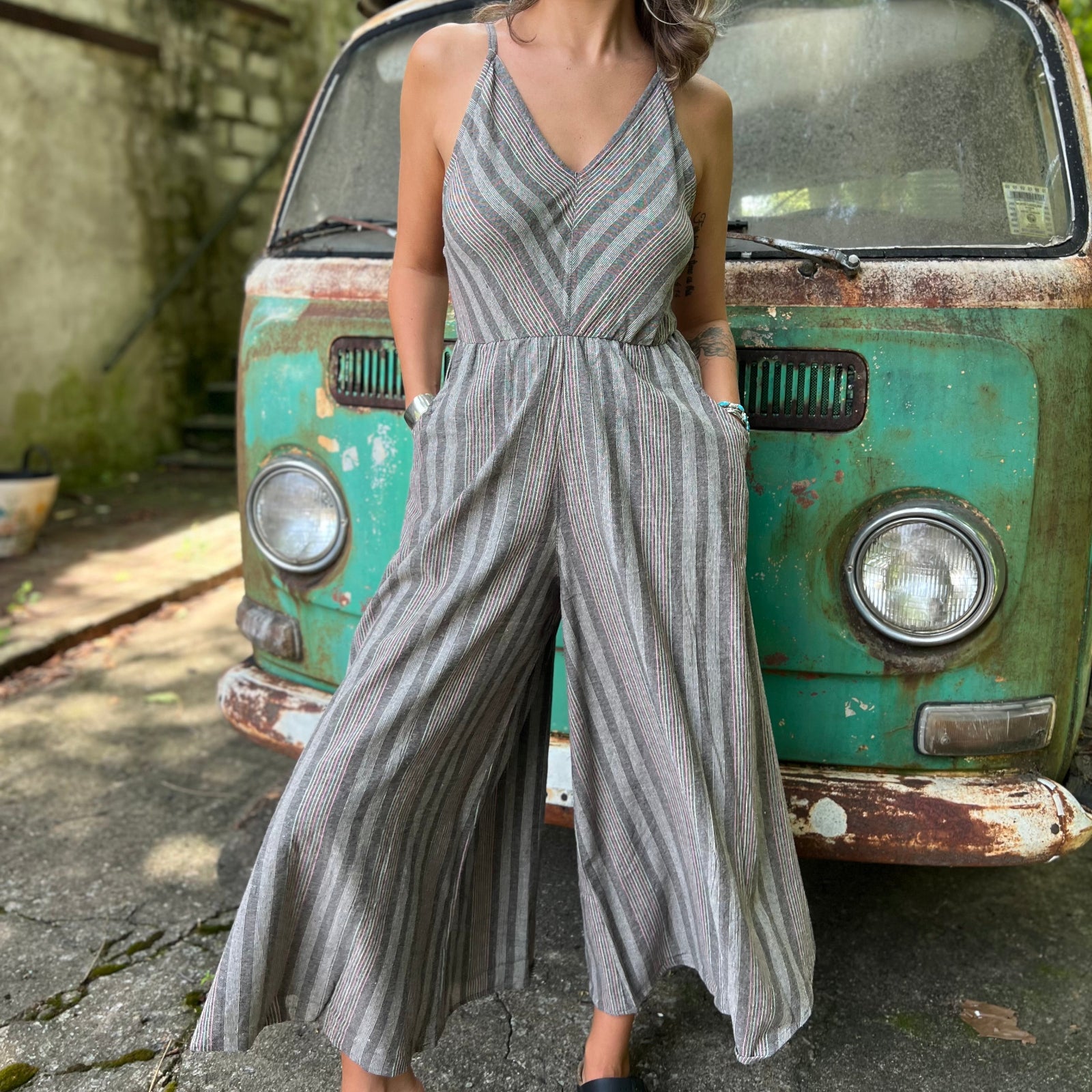 A woman wearing the Grey Striped Palazzo Cotton Jumpsuit in front of a vintage Volkswagen bus.