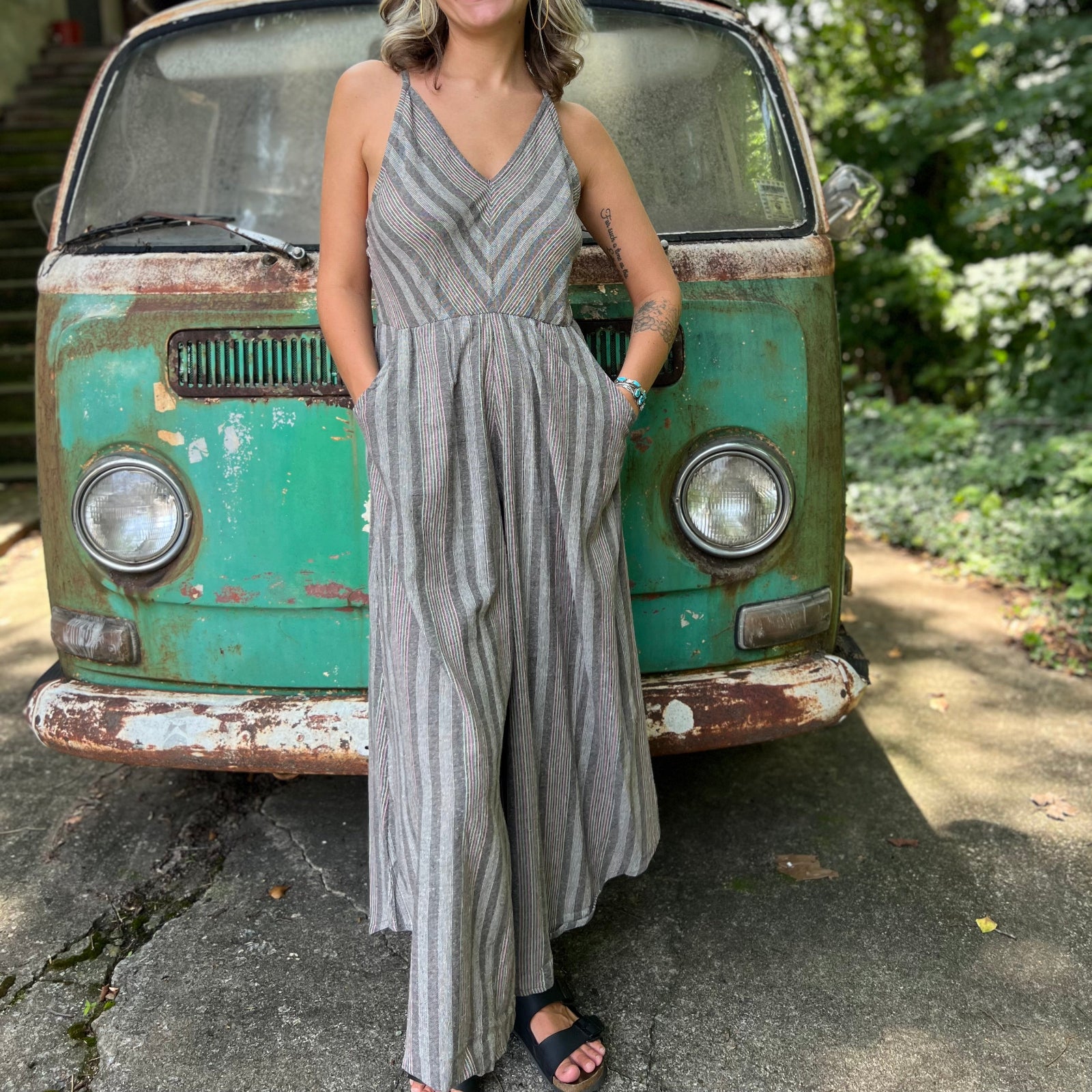 A woman wearing the Grey Striped Palazzo Cotton Jumpsuit in front of a vintage Volkswagen bus.