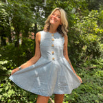 A woman wearing the Jeweled Button Denim Flare Cotton Dress oustide in front of some greenery.