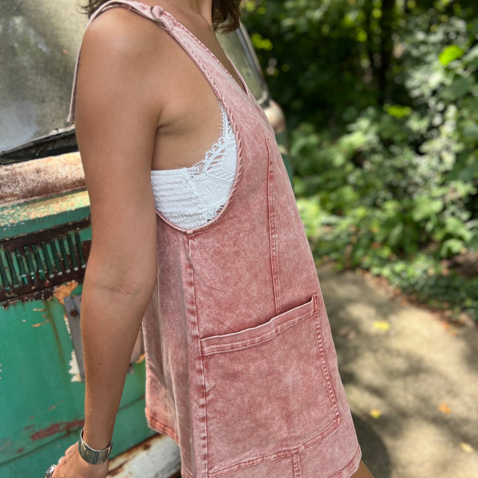 A woman wearing the Pink Garment Washed Cotton Denim Overall Dress in front of a vintage teal Volkswagen bus.
