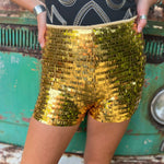 Someone wearing the Gold Sequin Fitted Hot Shorts with a black top in front o f a vintage Volkswagen bus.