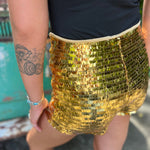 Someone wearing the Gold Sequin Fitted Hot Shorts with a black top in front o f a vintage Volkswagen bus.