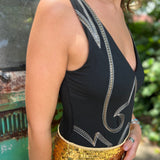 A woman wearing the Black Jersey Plunge Boots Stitch Bodysuit with gold shorts in front of a teal Volkswagen bus.