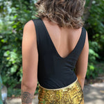 A woman wearing the Black Jersey Plunge Boots Stitch Bodysuit with gold shorts in front of a teal Volkswagen bus.