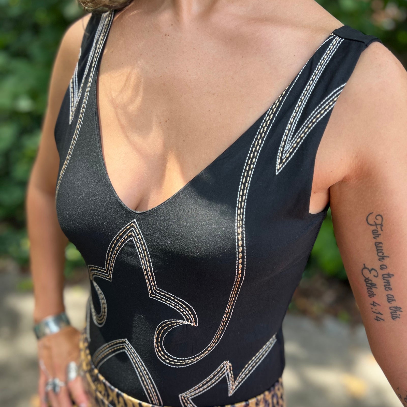 A woman wearing the Black Jersey Plunge Boots Stitch Bodysuit with gold shorts in front of a teal Volkswagen bus.