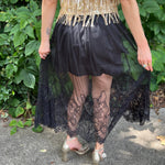 A woman wearing the Sheer Mesh Lace Mini Lined Maxi Skirt with a gold top in front of some greenery.
