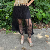 A woman wearing the Sheer Mesh Lace Mini Lined Maxi Skirt with a gold top in front of some greenery.