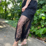 A woman wearing the Sheer Mesh Lace Mini Lined Maxi Skirt with a gold top in front of some greenery.