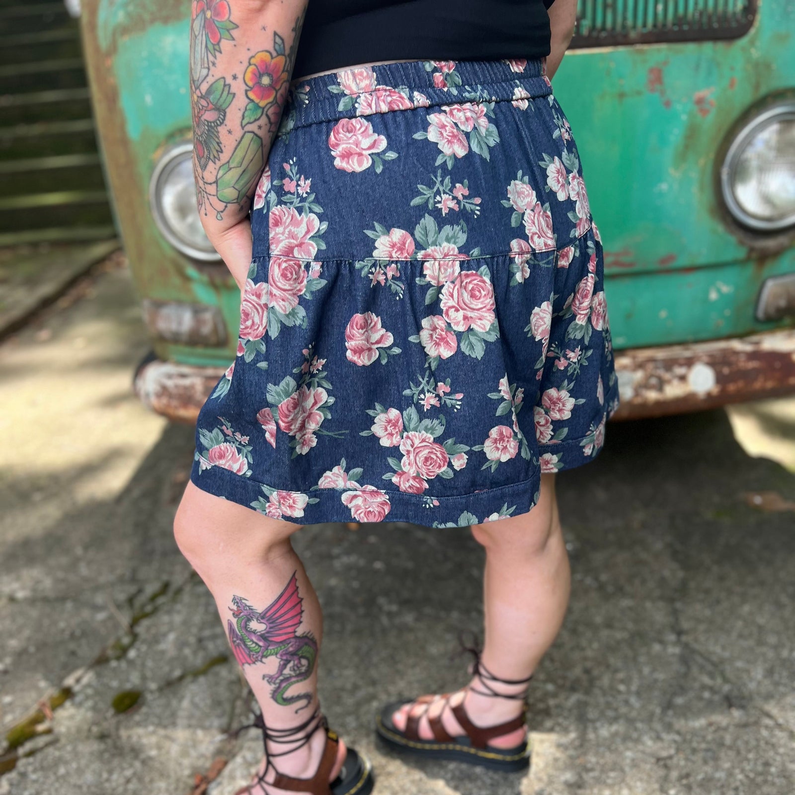 A woman wearing the Floral Print Denim Shorts in front of a teal vintage Volkswagen bus.