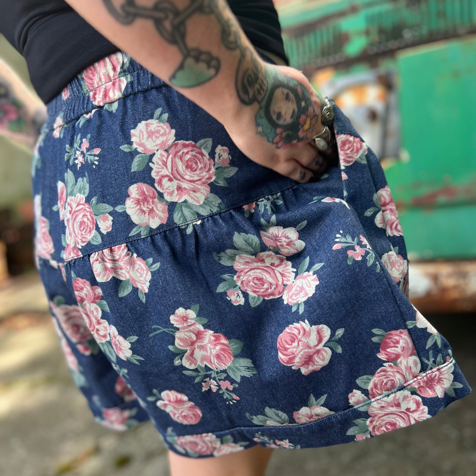 A woman wearing the Floral Print Denim Shorts in front of a teal vintage Volkswagen bus.