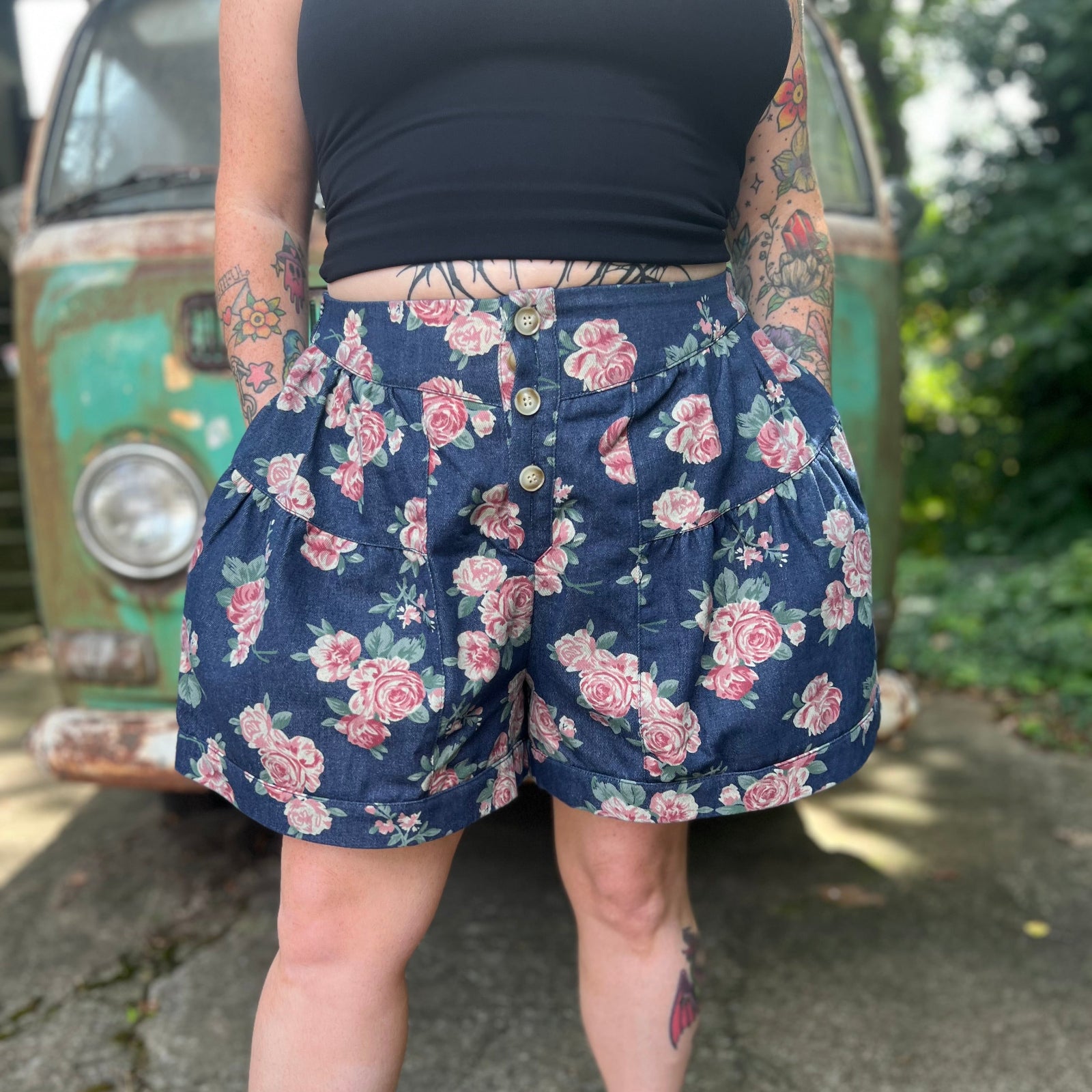 A woman wearing the Floral Print Denim Shorts in front of a teal vintage Volkswagen bus.