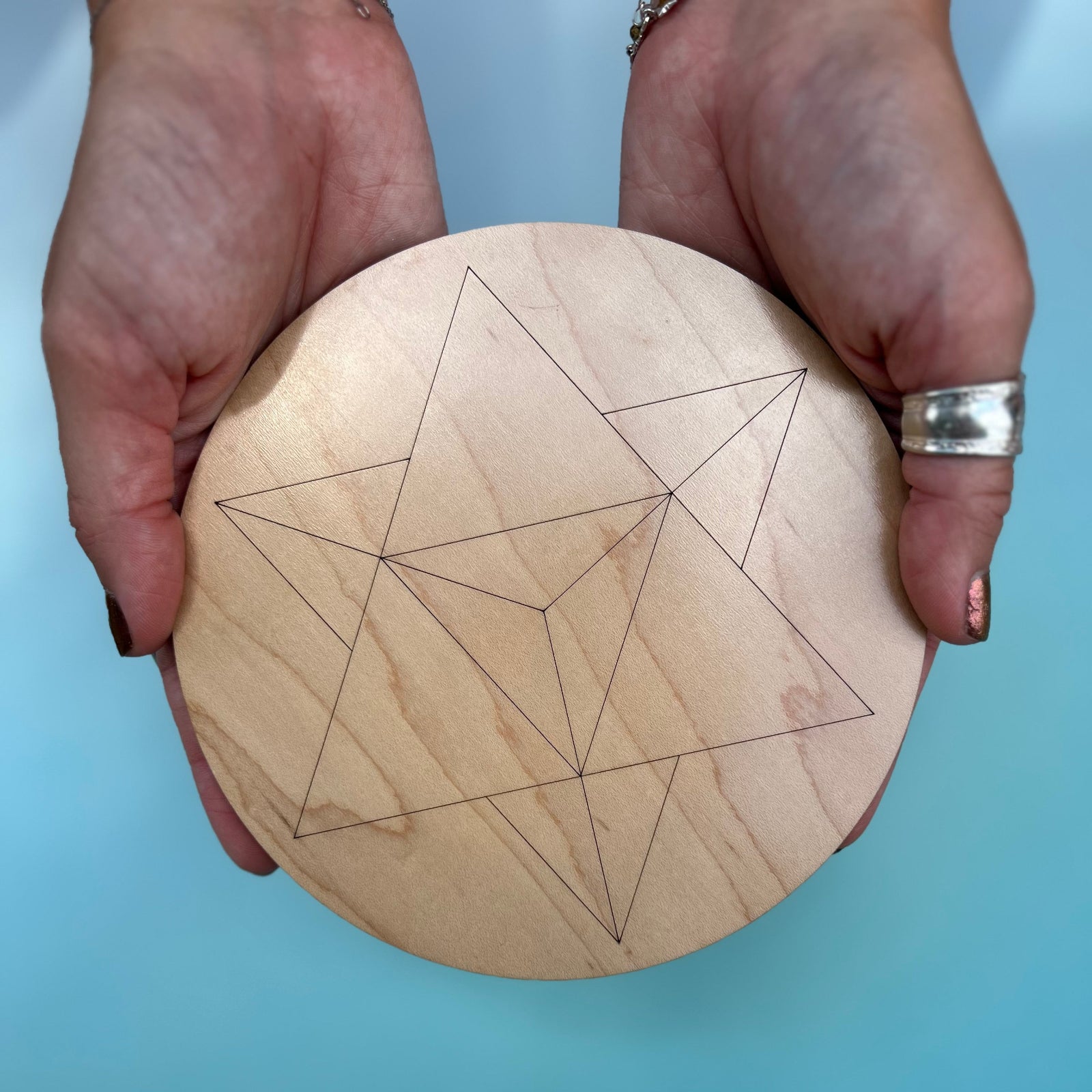 Someone holding the 6 inch Merkabah Wooden Crystal Grid in front of a blue background.