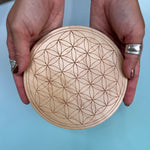 Someone holding the Flower of Life 6 inch Wooden Crystal Grid in front of a blue background.