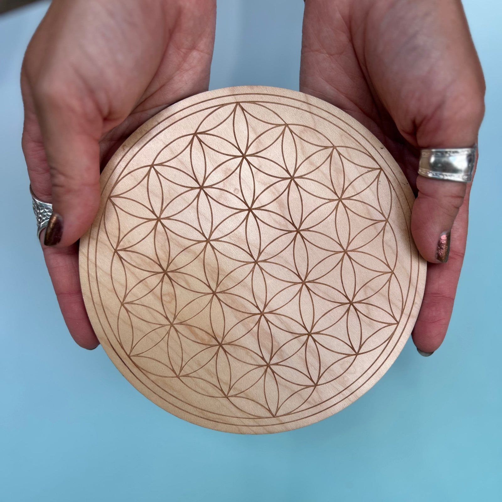 Someone holding the Flower of Life 6 inch Wooden Crystal Grid in front of a blue background.