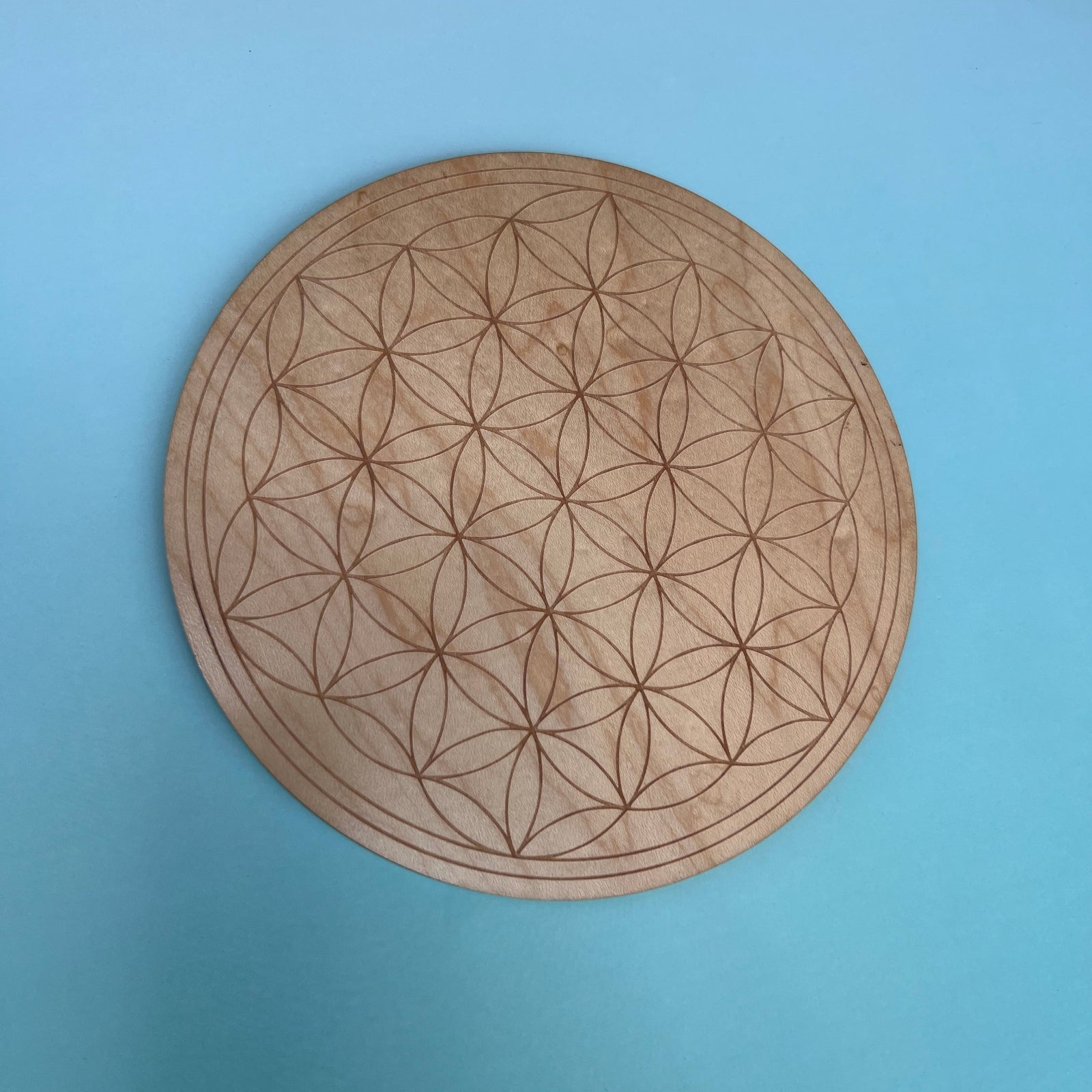 The Flower of Life 6 inch Wooden Crystal Grid on a light blue background.