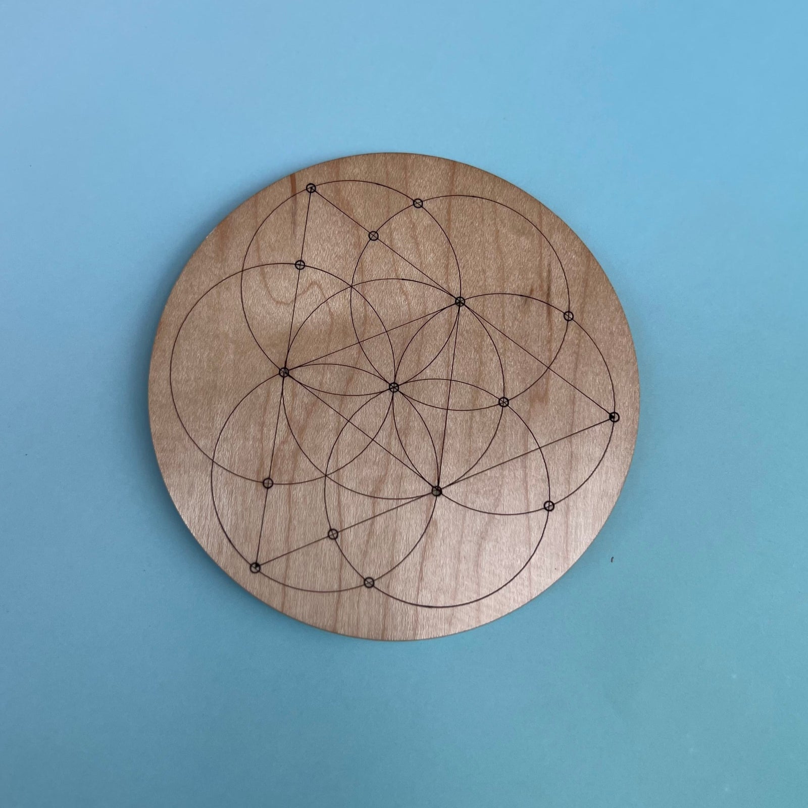 The Seed of Life 4 inch Wooden Crystal Grid on a light blue background.