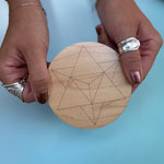 Someone holding the 4 inch Merkabah Wooden Crystal Grid in front of a blue background.