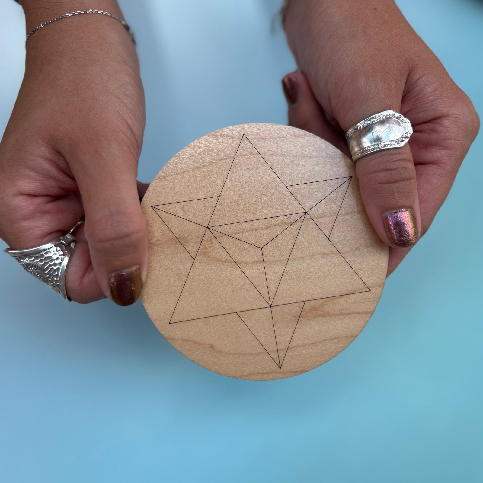 Someone holding the 4 inch Merkabah Wooden Crystal Grid in front of a blue background.