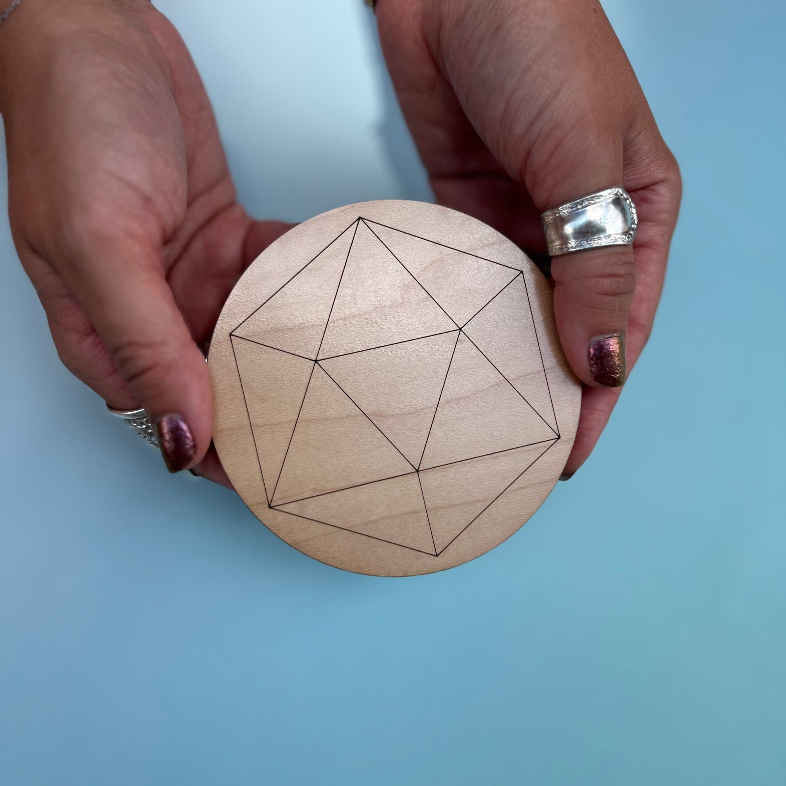 Someone holding the Icosahedron 4 inch Wooden Crystal Grid in front of a light blue background.
