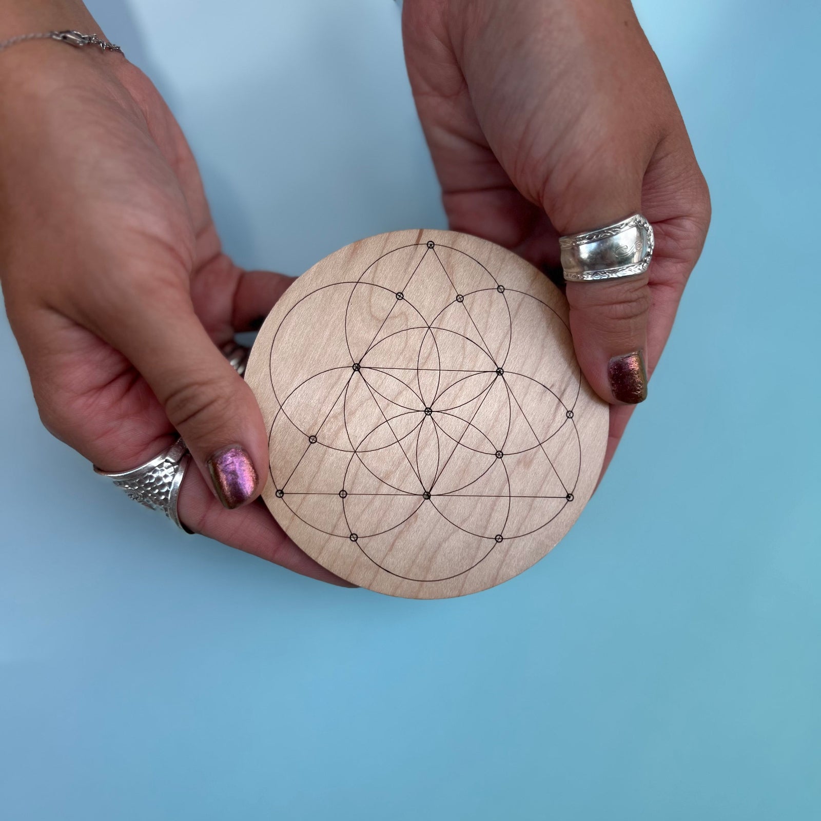 Someone holding the Seed of Life 4 inch Wooden Crystal Grid in front of a blue background.