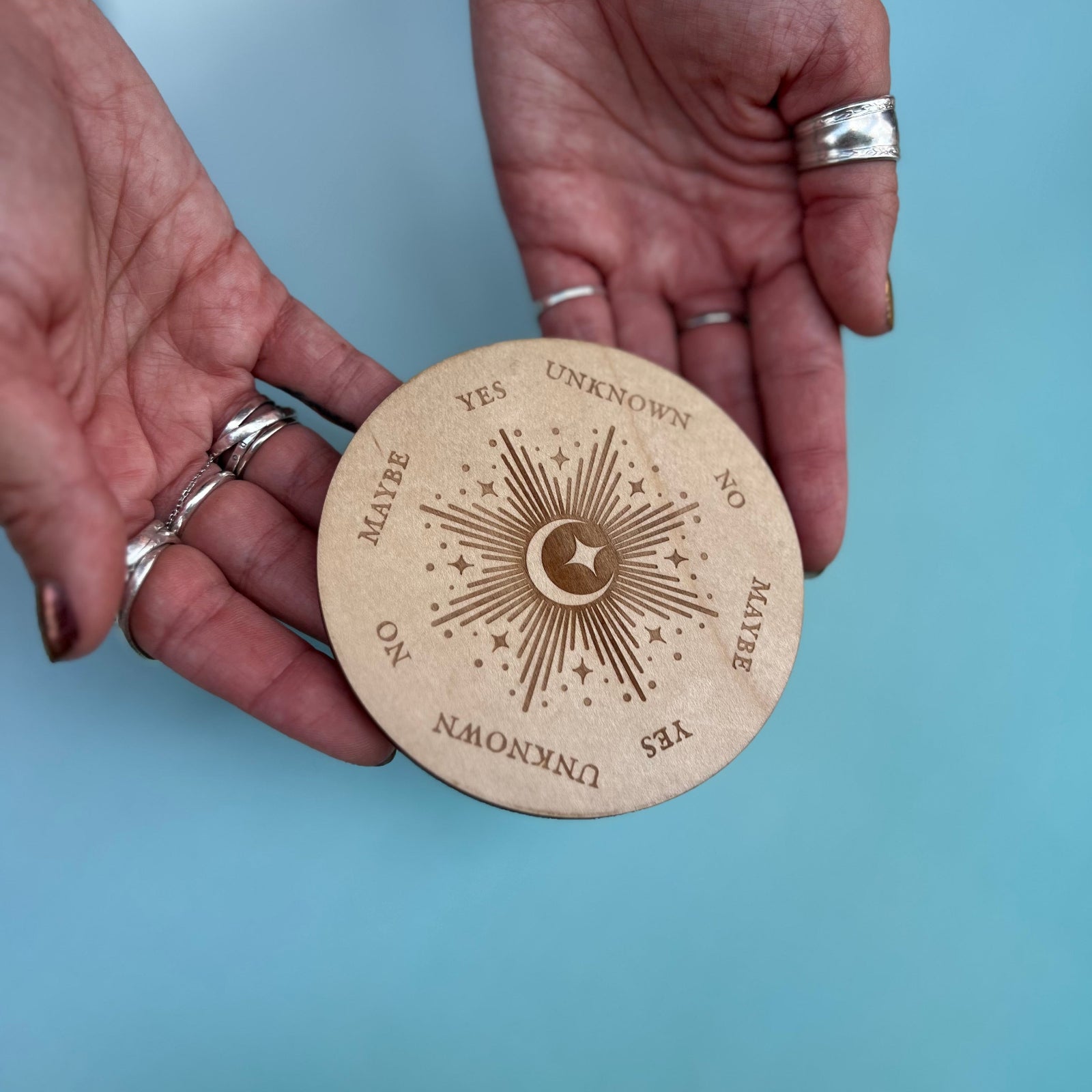 Someone holding the Moonlight Pendulum Wooden 4 inch Board in front of a blue background.