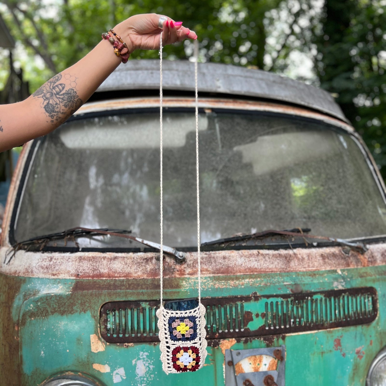 The Handmade Bohemian Crochet Phone Crossbody Bag being held in front of an old teal Volkswagen.