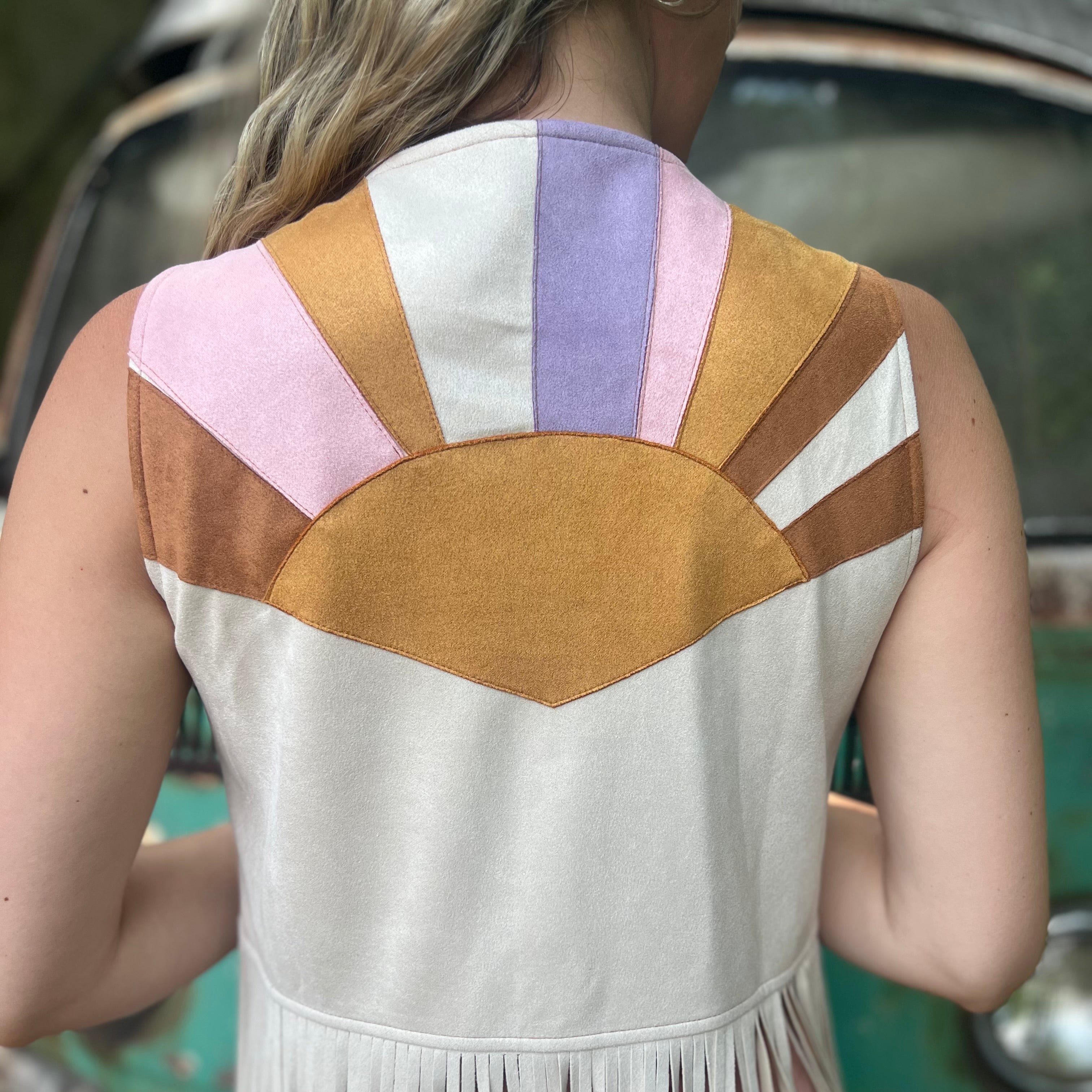 A woman wearing the cream Retro Sunburst Suede Color Block Long Fringe Faux Vest.