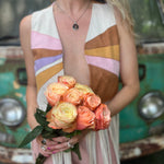 A woman wearing the cream Retro Sunburst Suede Color Block Long Fringe Faux Vest and holding a bouquet.
