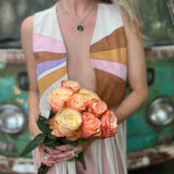 A woman wearing the cream Retro Sunburst Suede Color Block Long Fringe Faux Vest and holding a bouquet.