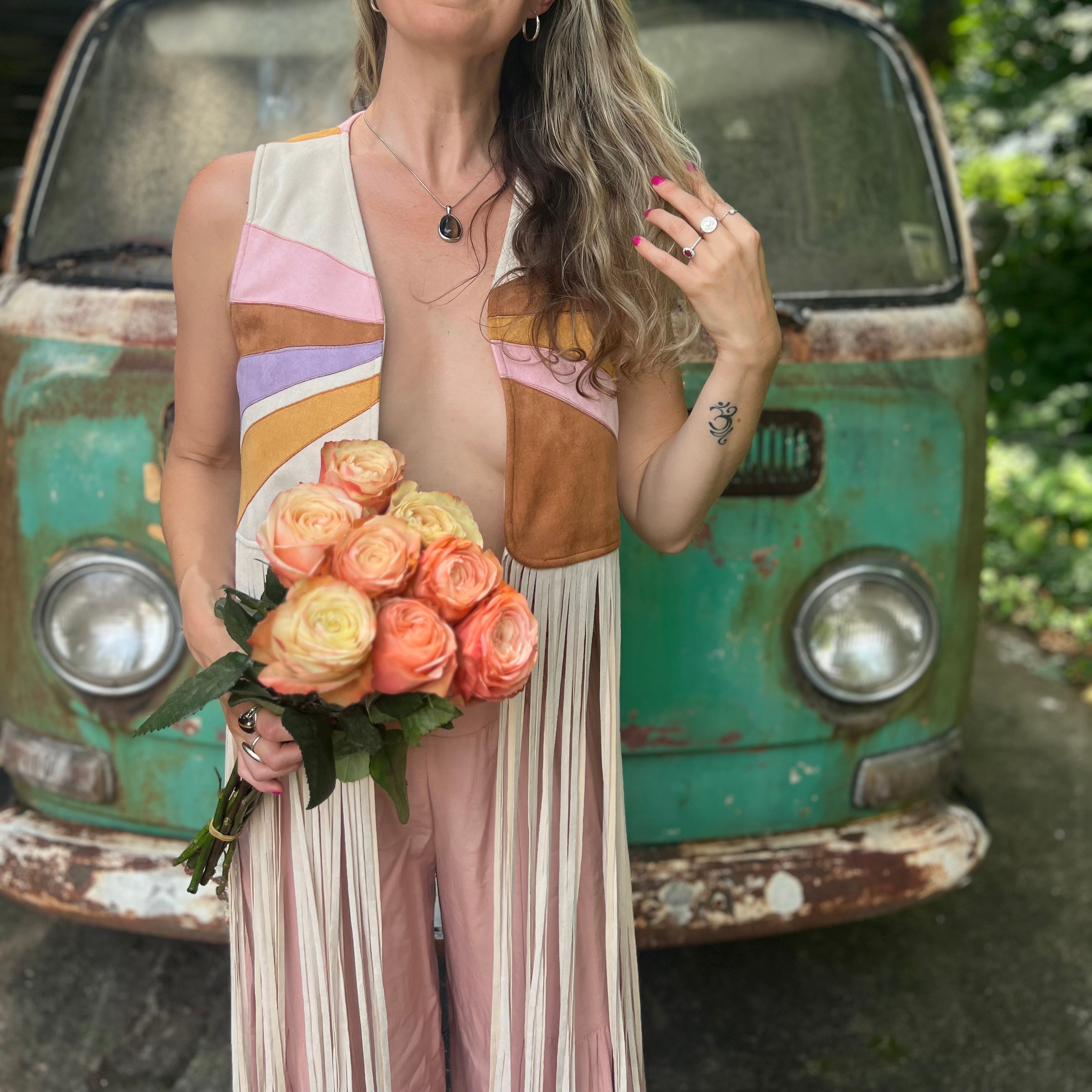 A woman wearing the cream Retro Sunburst Suede Color Block Long Fringe Faux Vest and holding a bouquet.