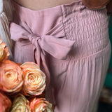 Someone wearing the mauve Smocking Waist Tier Wide Pants with flowers next to them.
