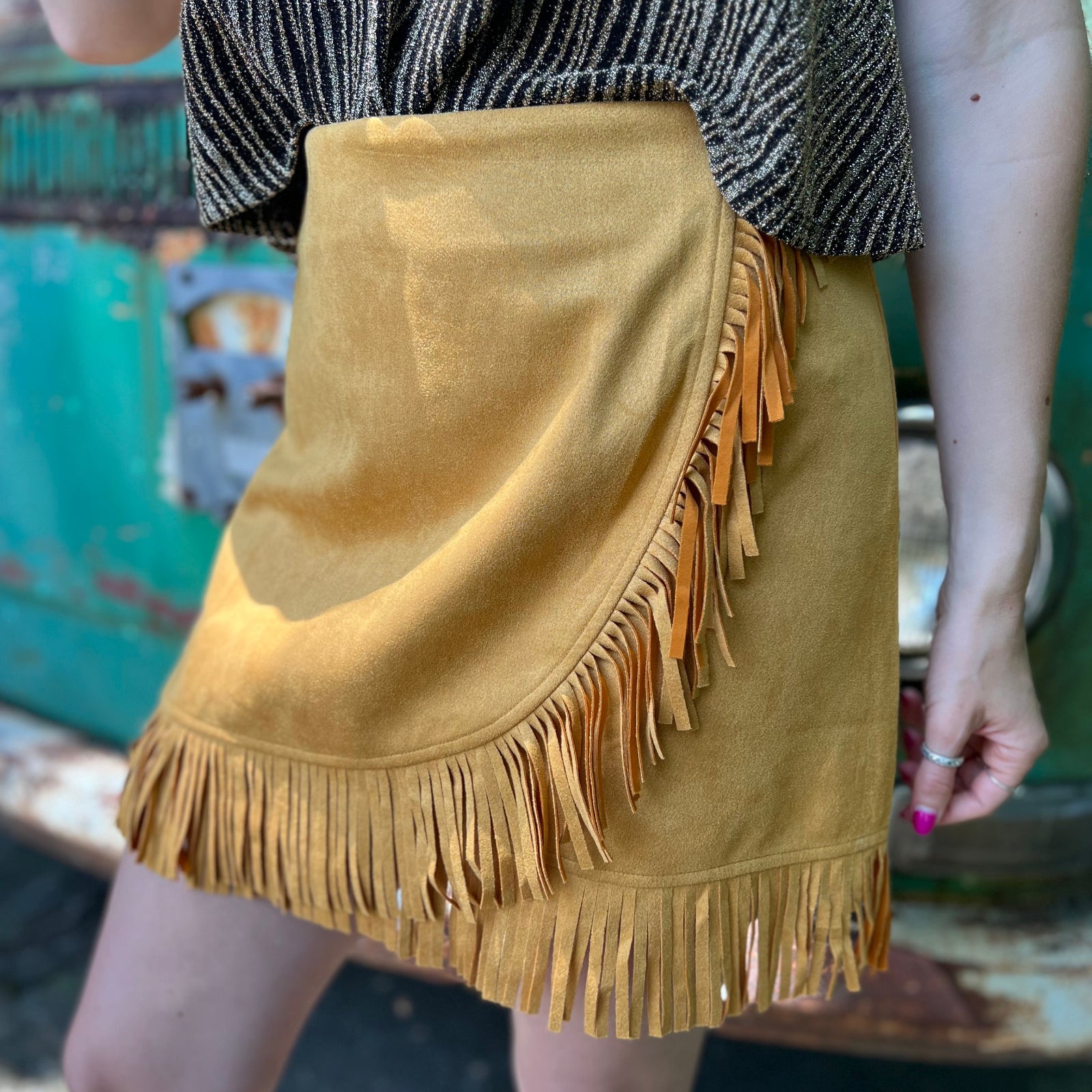 A woman wearing the Mustard Suede Fringe Wrap Skirt with a sparkly top.