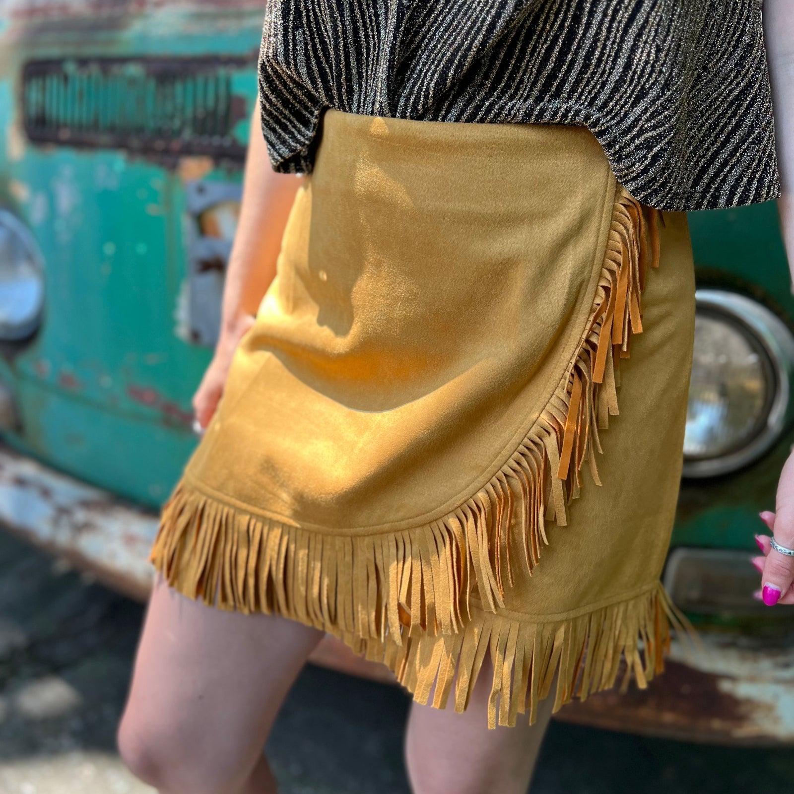 A woman wearing the Mustard Suede Fringe Wrap Skirt with a sparkly top.