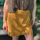 A woman wearing the Mustard Suede Fringe Wrap Skirt with a sparkly top.