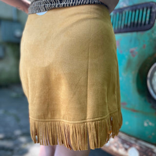 A woman wearing the Mustard Suede Fringe Wrap Skirt with a sparkly top.