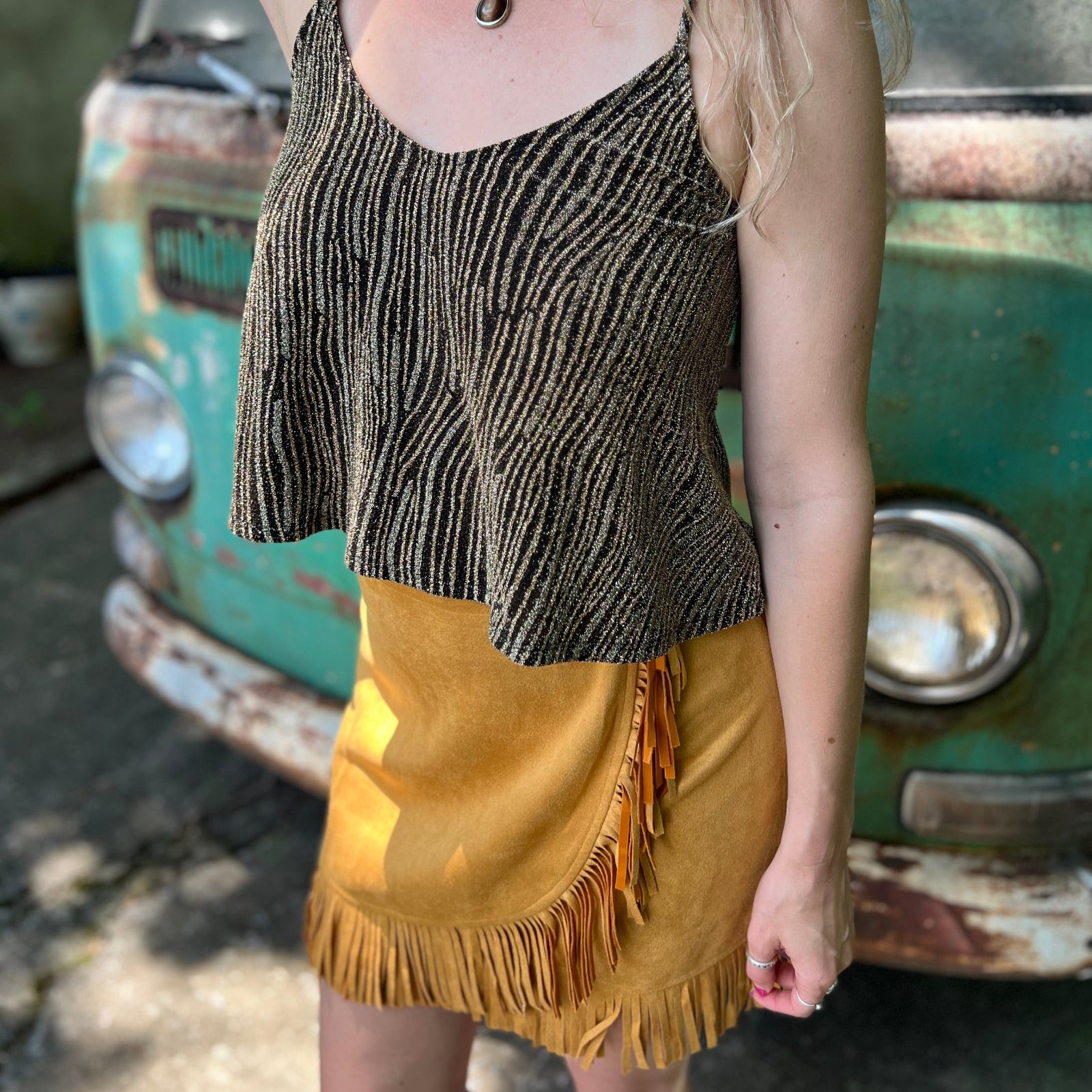 A woman wearing the Mustard Suede Fringe Wrap Skirt with a sparkly top.