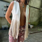 A woman wearing the cream Western Open Soft Suede Fringe Vest with red patterned pants.