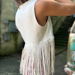 A woman wearing the cream Western Open Soft Suede Fringe Vest with red patterned pants.