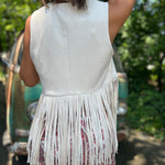 A woman wearing the cream Western Open Soft Suede Fringe Vest with red patterned pants.