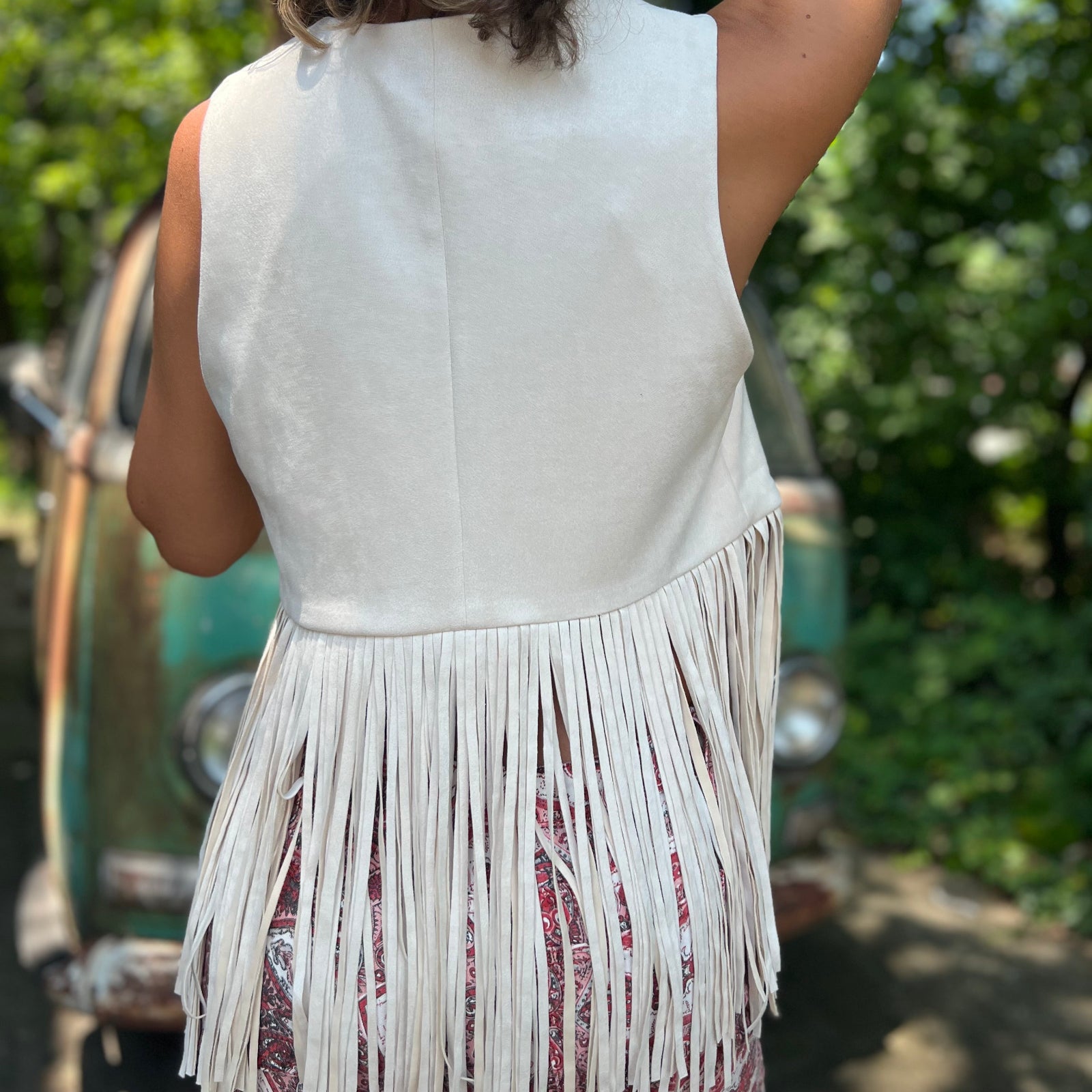 A woman wearing the cream Western Open Soft Suede Fringe Vest with red patterned pants.
