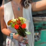 A woman wearing the cream Western Open Soft Suede Fringe Vest with red patterned pants holding flowers.