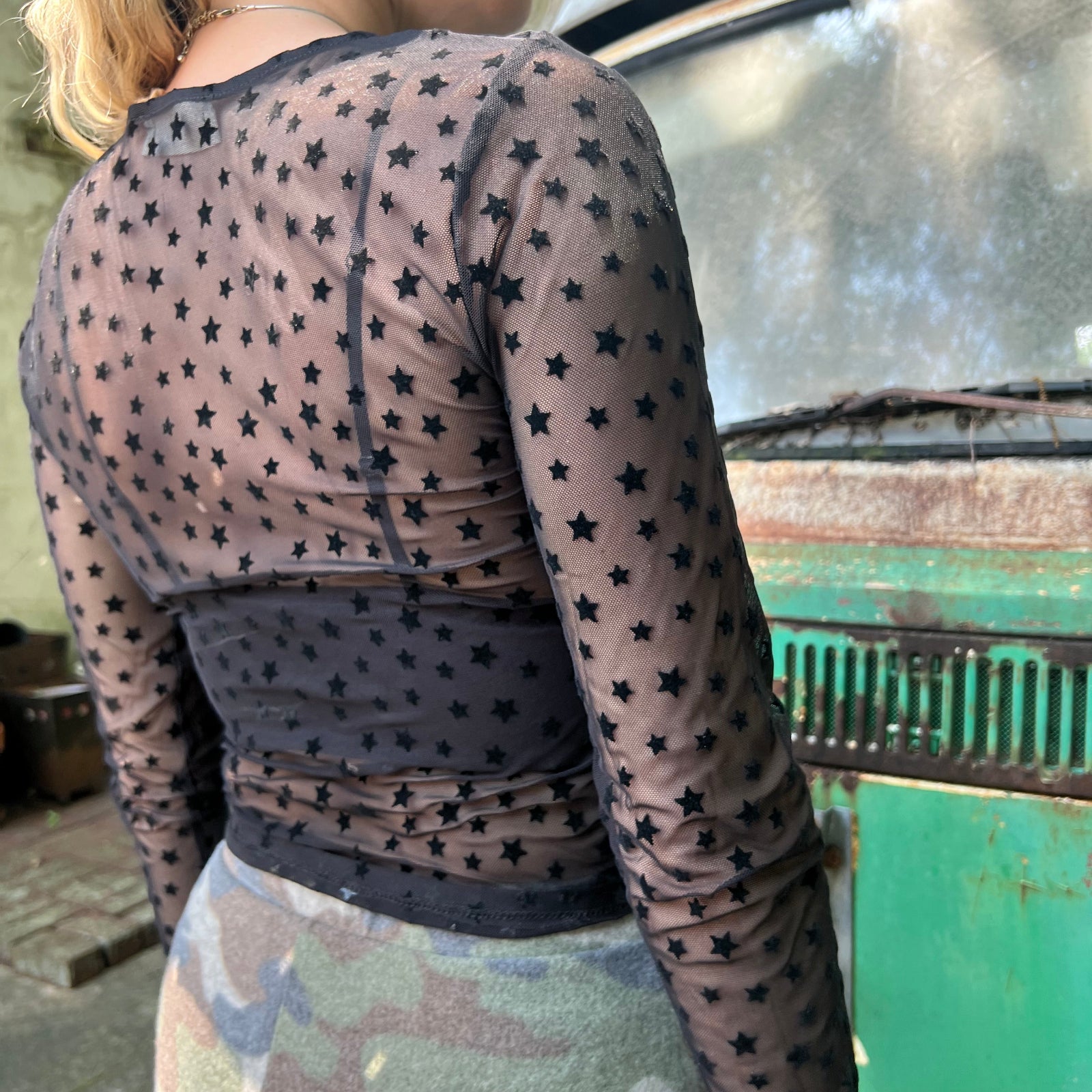 A woman wearing the Star Flocking Sheer Mesh Top and a camo skirt.