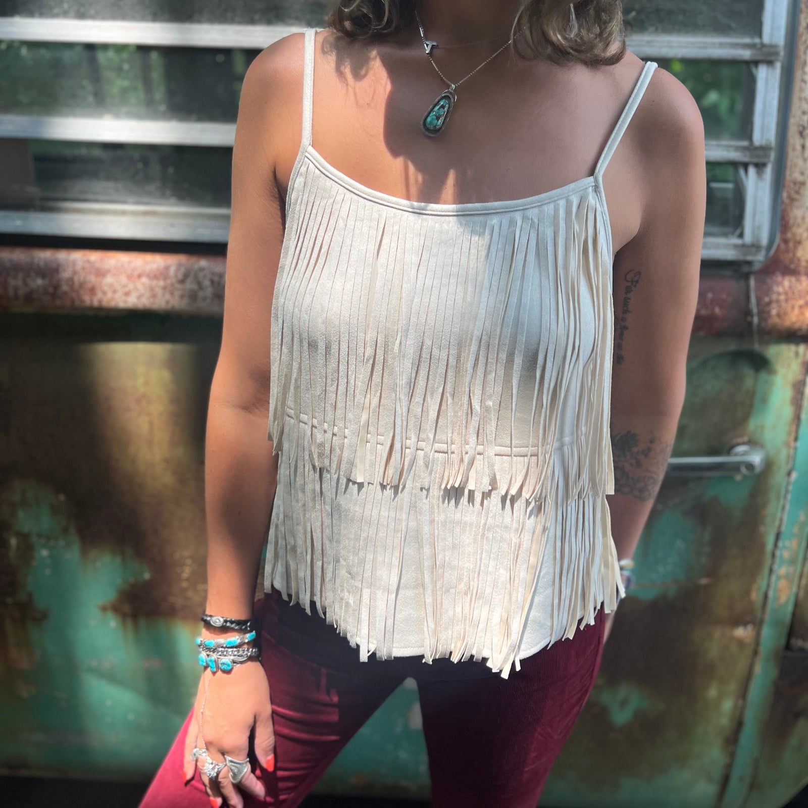 A woman wearing the Cream Fringe Faux Suede Cami with wine bell bottoms.